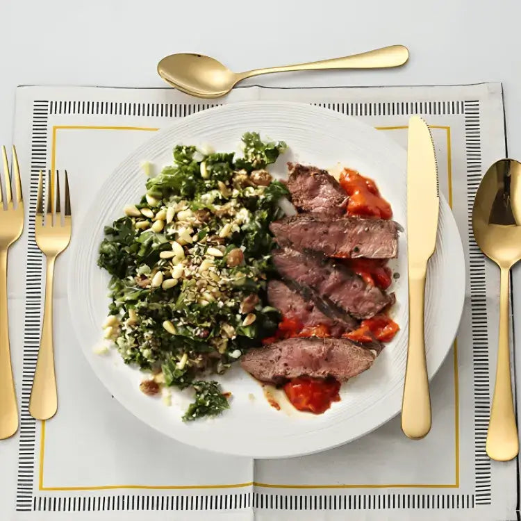 jogo-de-talheres-dourado-em-inox-modernize-foto-talheres-ao-redor-de-prato-sobre-guardanapo-com-alimentos